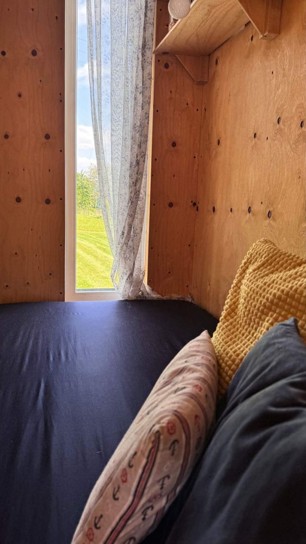 Lůžko s polštáři pod oknem se záclonkou